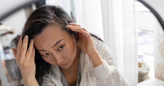 Woman checking grey hair roots in the mirror before using hair dye shampoo