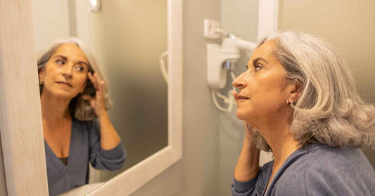woman noticing first gray hair near temples in mirror
