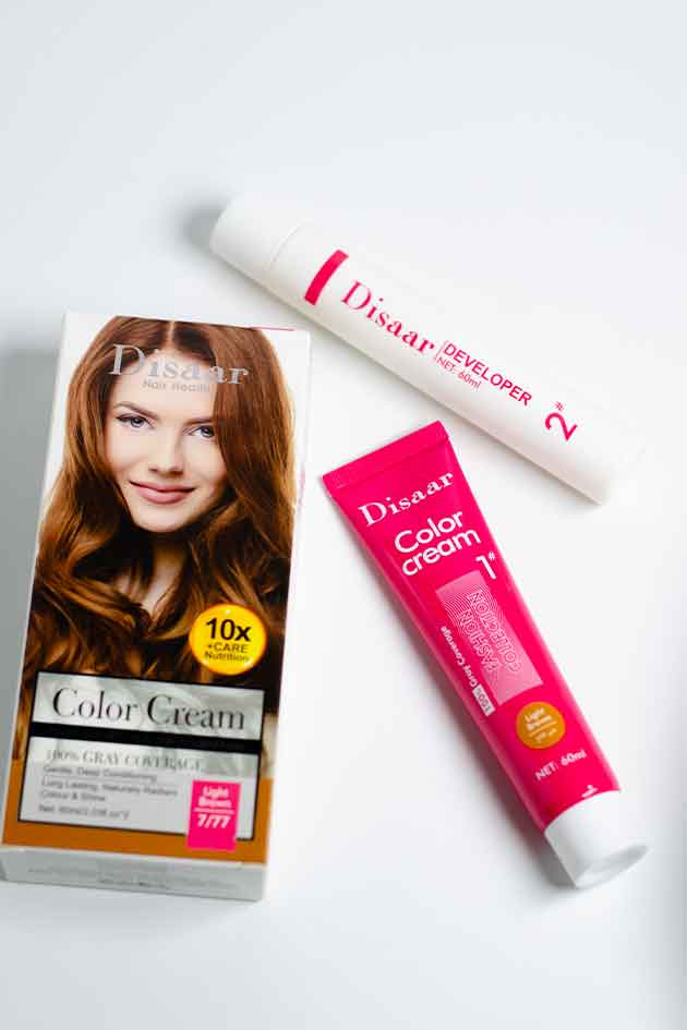 Applying Disaar Light Brown hair dye for smooth, even, and shiny results. Dissaar hair color products including a packet, tube, and developer on a beige background. Dissan hair color cream packaging with a woman's face on it, on a white background.