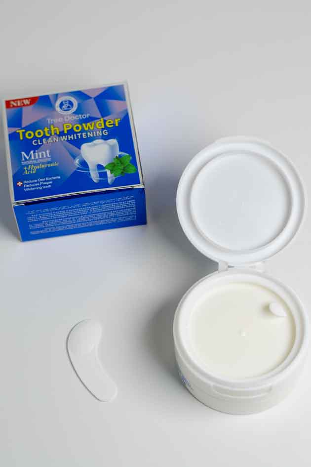 Open container of tooth powder with packaging on a white background