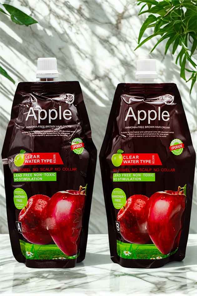 Ammonia-free apple hair color cream with no scalp irritation and 96-hour fragrance. Two Apple juice pouches on a marble surface with a blurred green leafy background