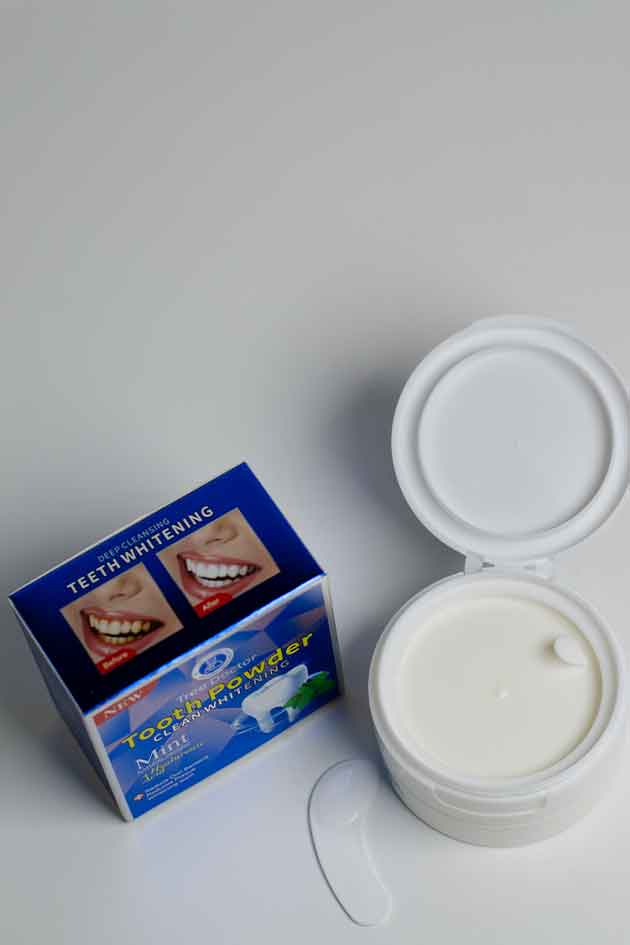 Open container of teeth whitening powder with packaging on a white background