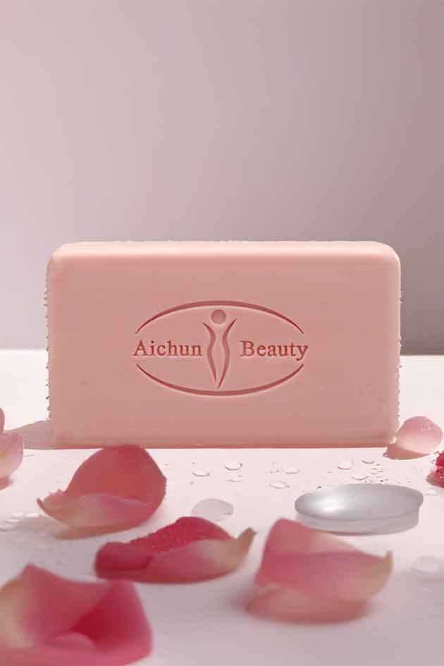 Pink bar of soap with 'Aichun Beauty' branding on a white surface with pink petals.