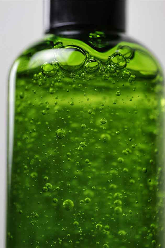 Close-up of a green liquid in a bottle with bubbles on a light gray background